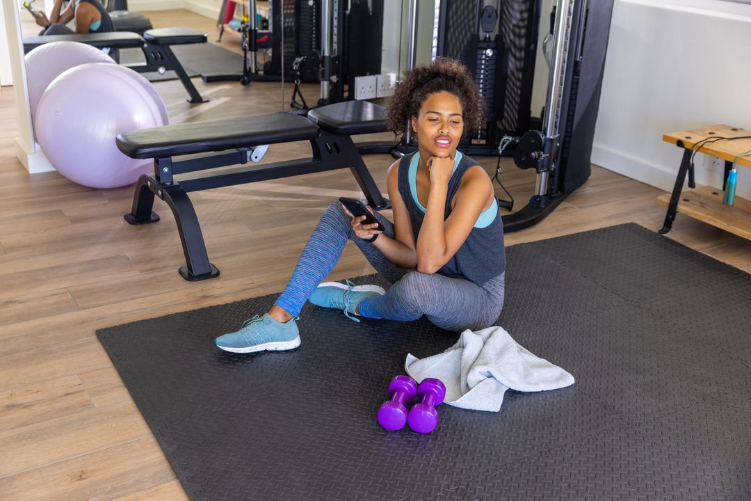 Woman Relaxing on Mat with Weights and Smartphone in Home Gym