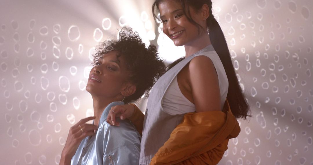 Diverse female duo posing in satin bomber and mustard jacket with warm lens flare