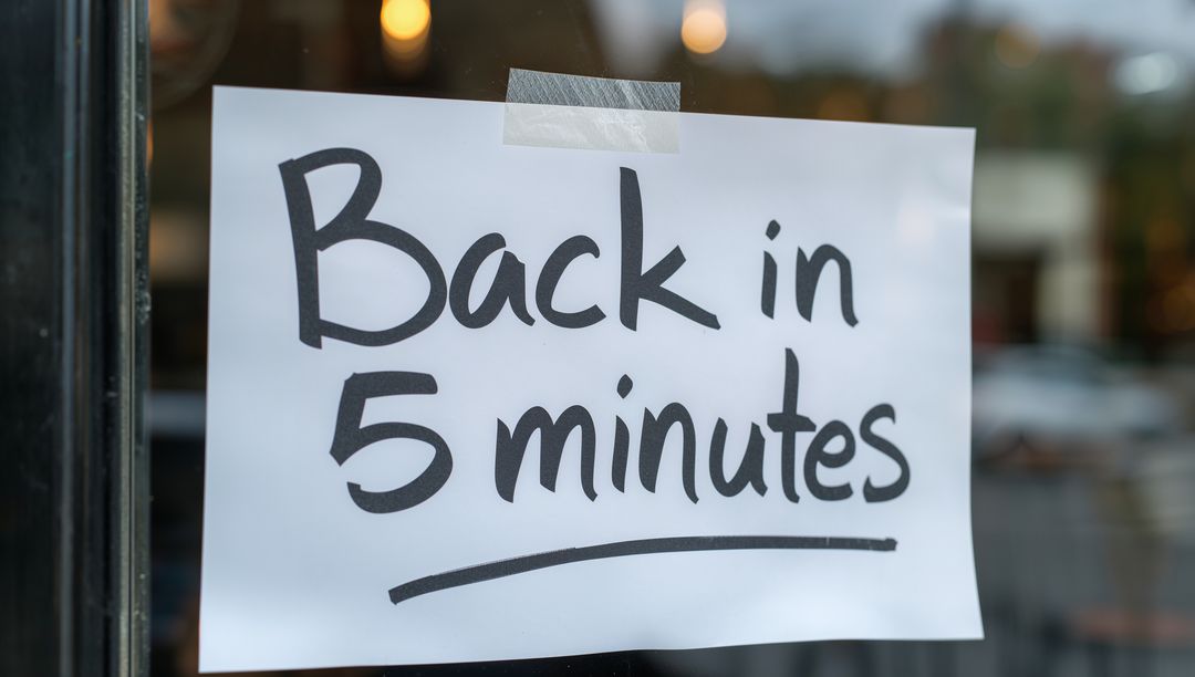 Showing handwritten Back in 5 minutes sign on glass door with blurred interior lights