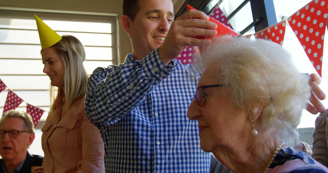 Son Assisting Elderly Mother with Party Hat at joyful Celebration - Free Images, Stock Photos and Pictures on Pikwizard.com