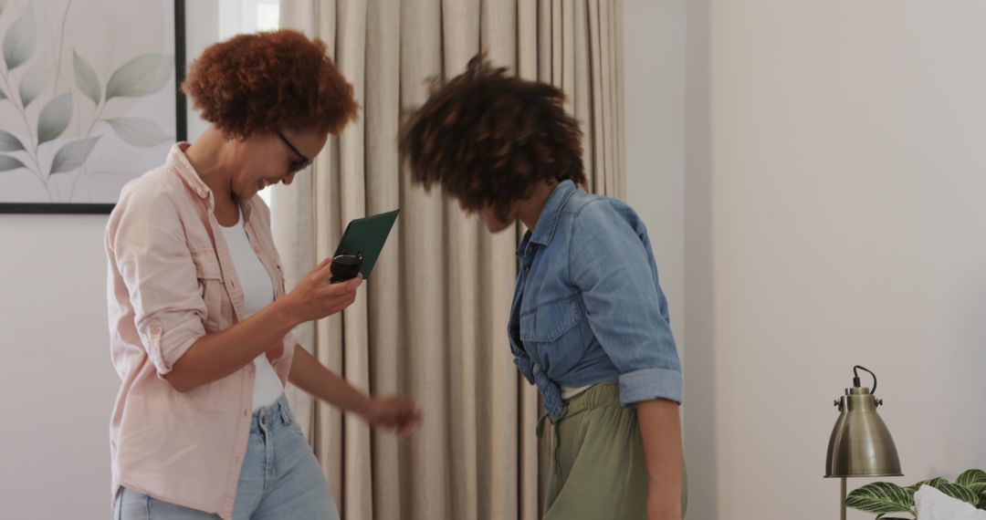 Midlife Friends Dancing and Bobbing Heads at Home Holding Smartphone and Folder