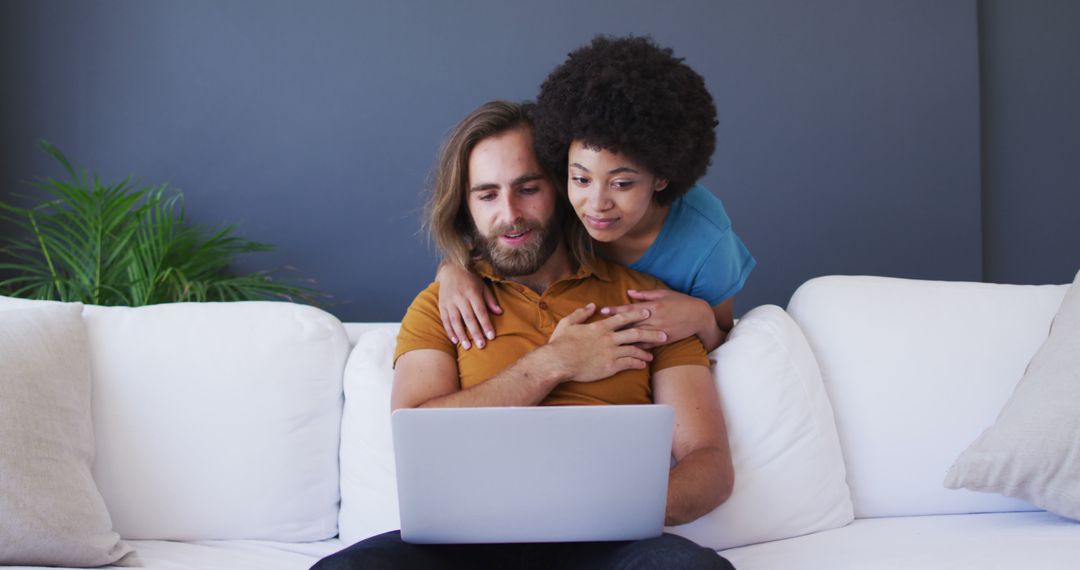 Biracial couple looking at laptop and embracing in living room - Free Images, Stock Photos and Pictures on Pikwizard.com