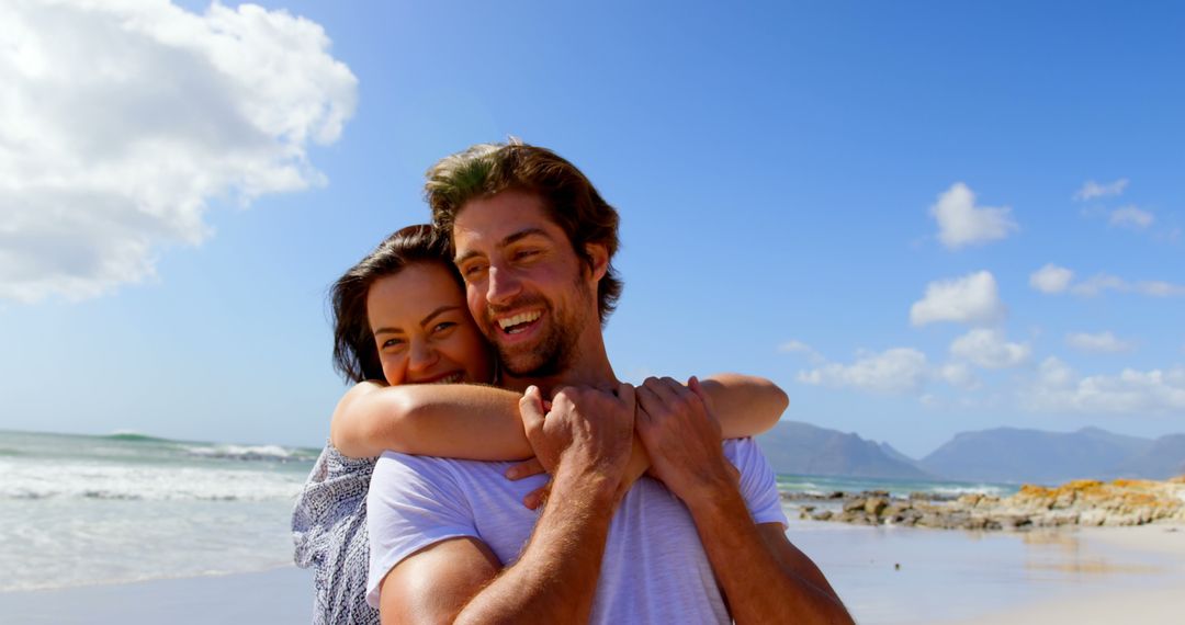 Happy Couple Embracing on Scenic Beach with Mountains - Free Images, Stock Photos and Pictures on Pikwizard.com