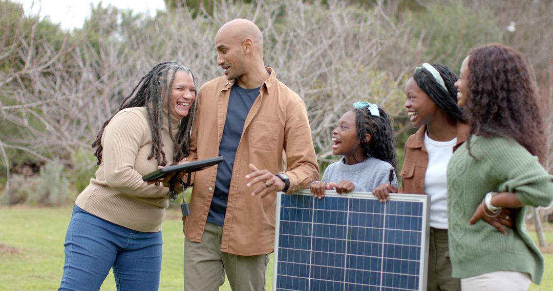 Black Family Exploring Portable Solar Panel While Laughing and Learning on Park Lawn