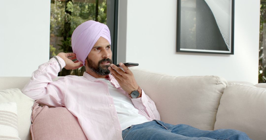 Relaxed Man in Turban Using Smartphone Mouthpiece on Couch