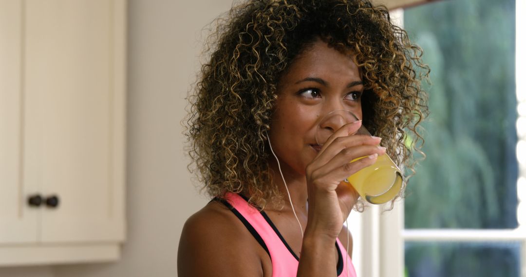 Woman with Curly Hair Drinking Orange Juice and Listening to Music - Free Images, Stock Photos and Pictures on Pikwizard.com