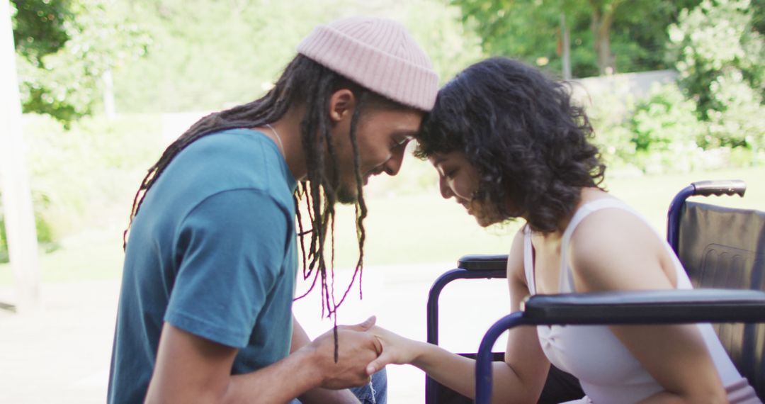 Biracial couple touching heads holding hands in garden, woman in wheelchair, man with dreadlocks - Free Images, Stock Photos and Pictures on Pikwizard.com