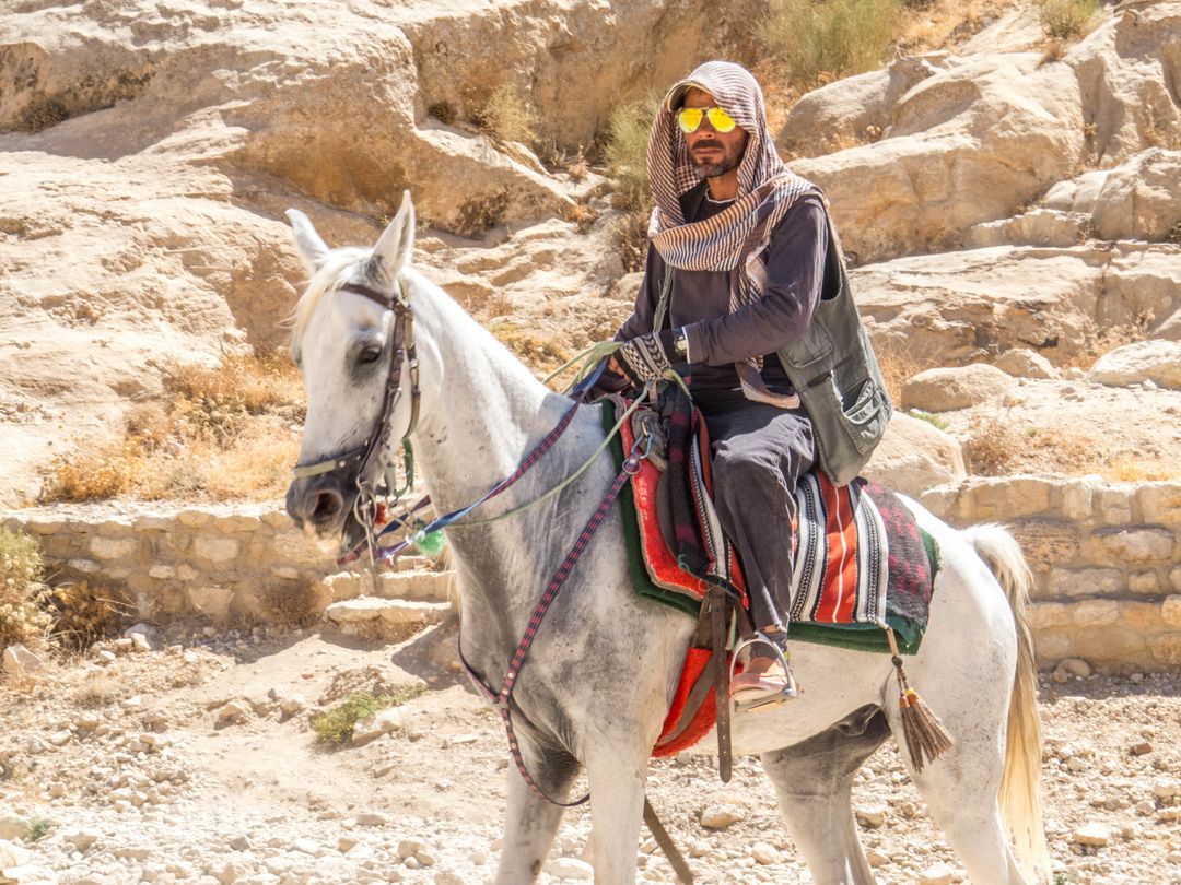Man Riding Horse in Desert with Traditional Garb in Sunlight
