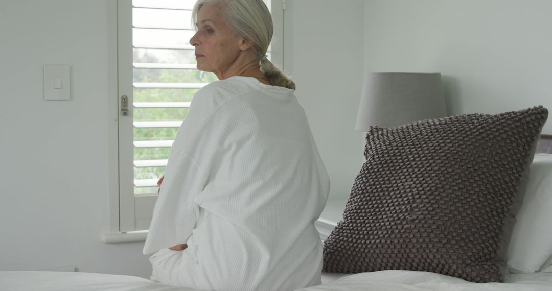 Senior Woman Reflecting by Window in Cozy White Bedroom - Free Images, Stock Photos and Pictures on Pikwizard.com