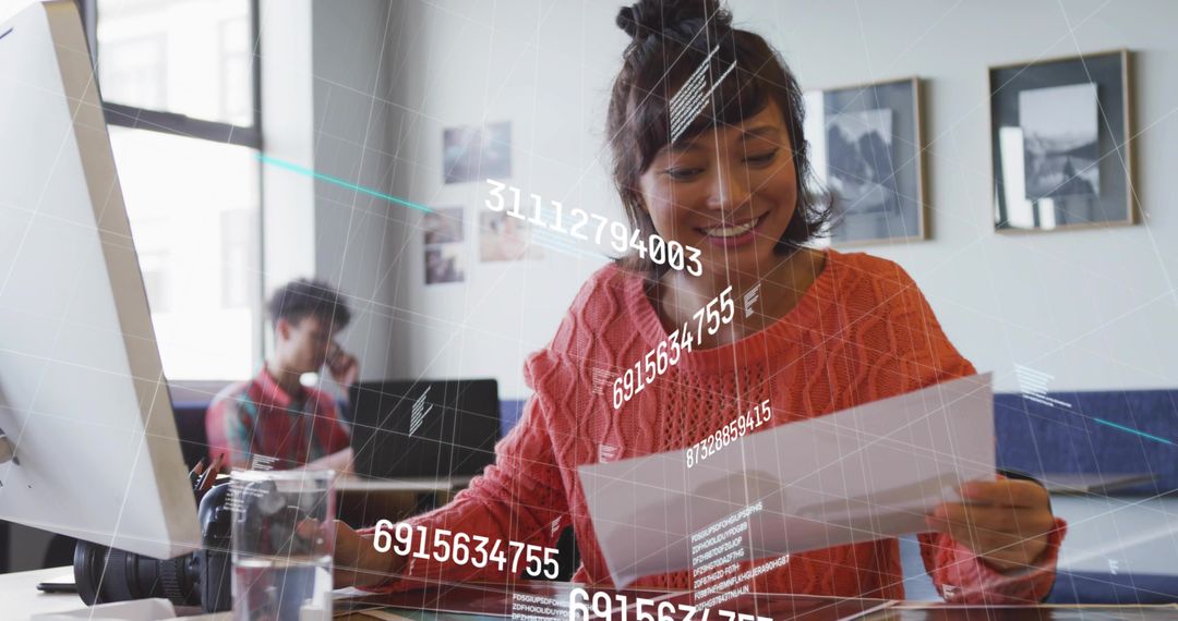 Young woman reading document smiling at modern coworking desk with data overlay