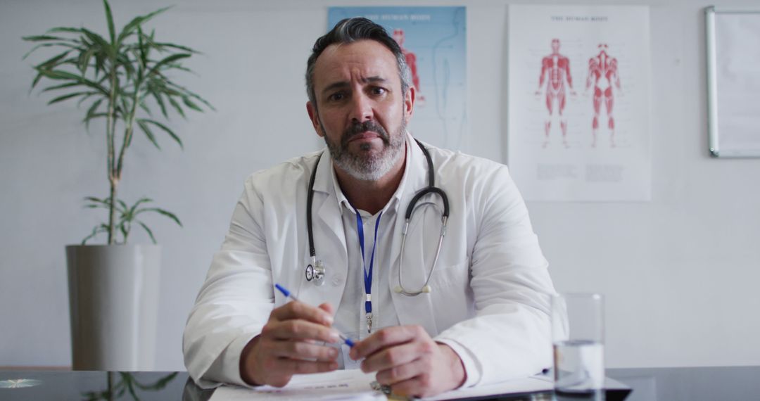 Male Doctor Sitting in Office with stethoscope holding a pen - Free Images, Stock Photos and Pictures on Pikwizard.com