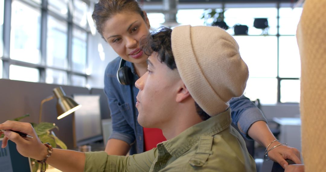 Colleagues collaborating and mentoring on laptop in modern open-plan office with daylight