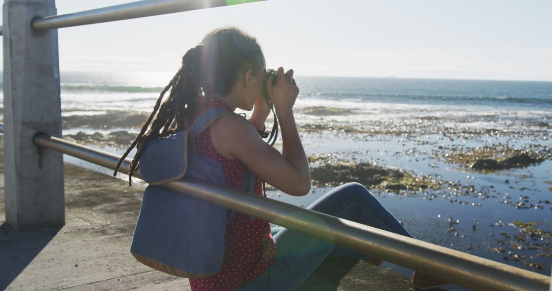 Young Woman Sitting by the Ocean Observing with Binoculars - Free Images, Stock Photos and Pictures on Pikwizard.com