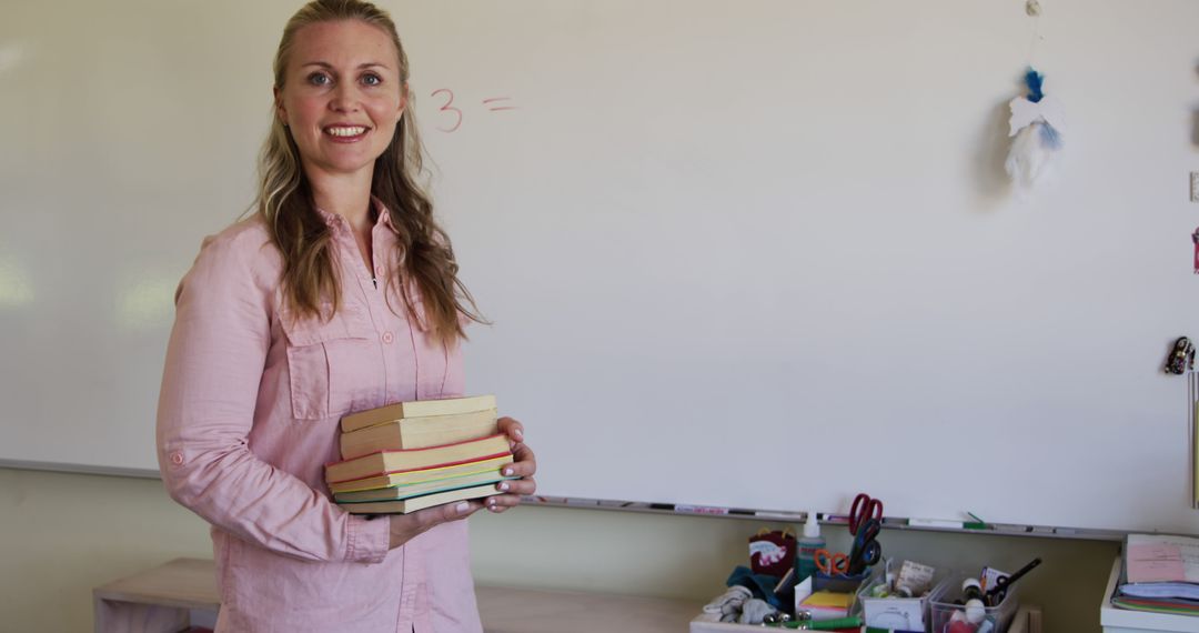 Smiling Female Teacher Holding Books in Classroom with Whiteboard - Free Images, Stock Photos and Pictures on Pikwizard.com