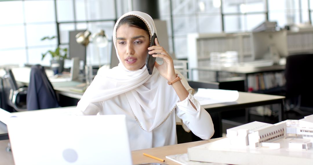 Woman in Hijab Talking on Phone Working on Laptop in Office