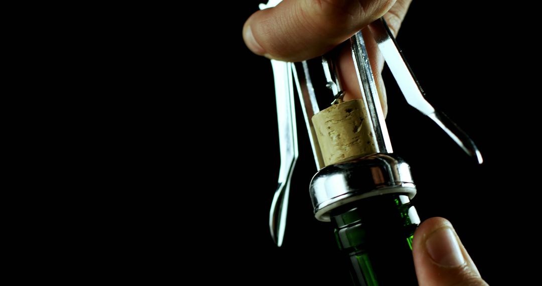 Hand Using Wing Corkscrew to Open Wine Bottle Against Black Background