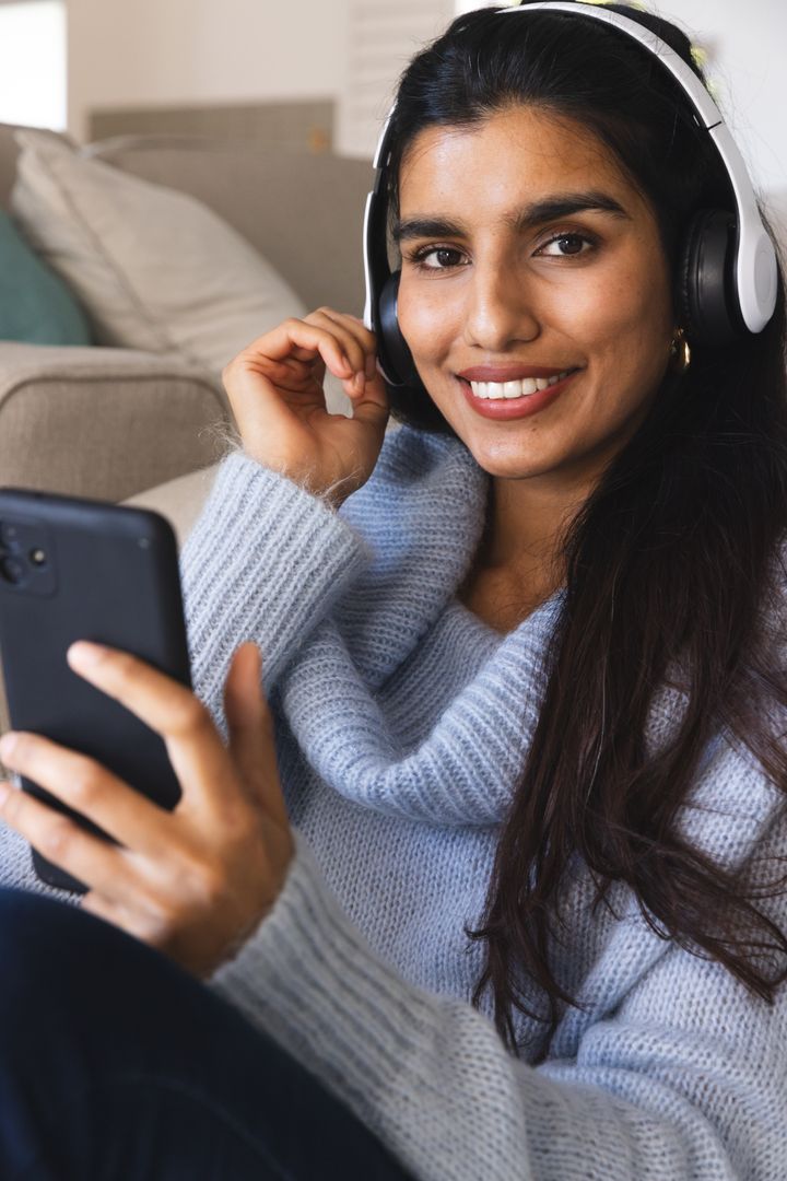 Smiling South Asian Woman Taking Selfie with Headphones and Smartphone at Home
