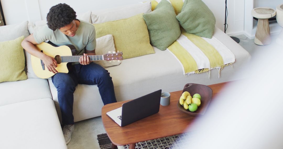 Young Man Playing Guitar While Using Laptop at Home