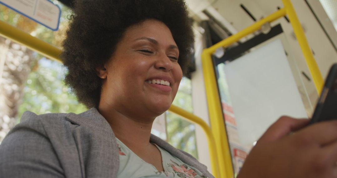 Smiling Woman with Curly Hair Using Smartphone on Bus