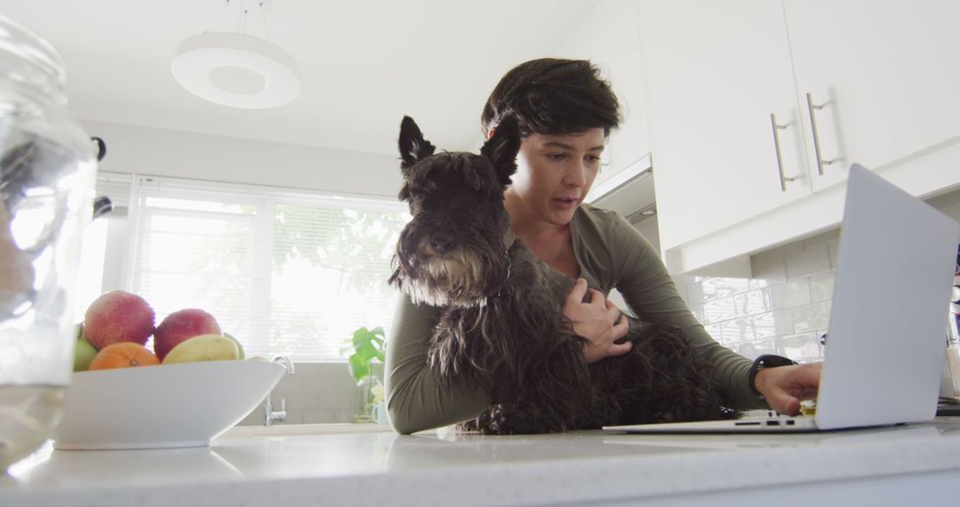 Caucasian woman holding her dog and using laptop at home - Free Images, Stock Photos and Pictures on Pikwizard.com