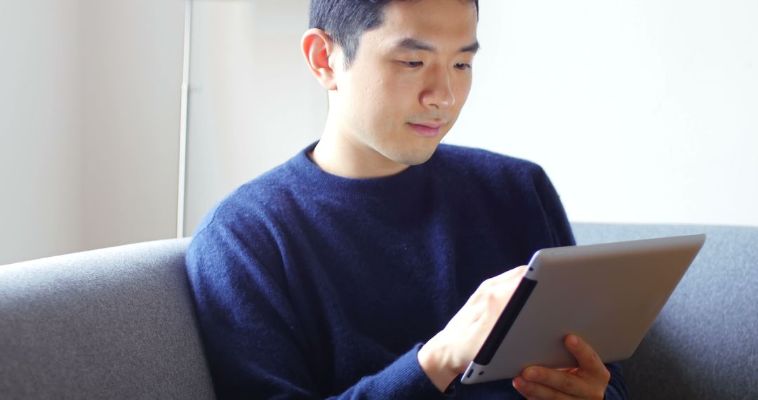 Young Man Sitting on Couch Using Tablet for Work - Free Images, Stock Photos and Pictures on Pikwizard.com