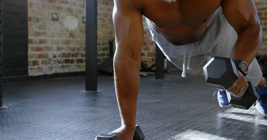 Athletic man performing push-up with dumbbells in gym - Free Images, Stock Photos and Pictures on Pikwizard.com