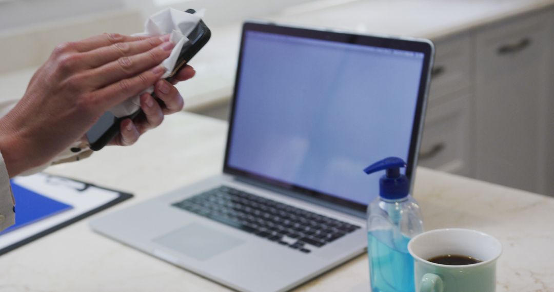 Person Cleaning Smartphone Next to Laptop and Antibacterial Spray in Office - Free Images, Stock Photos and Pictures on Pikwizard.com