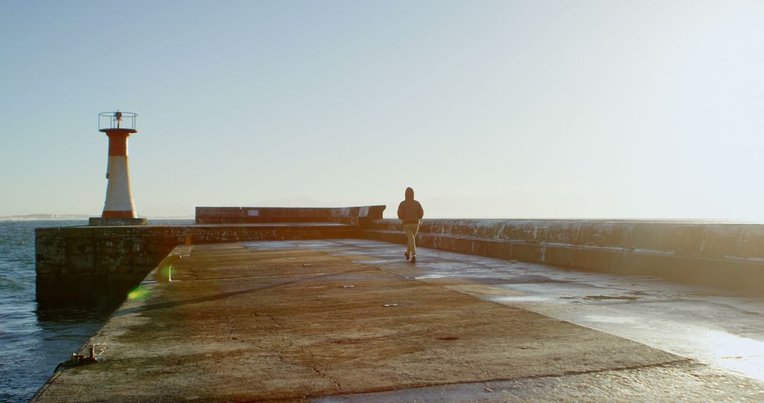 Person Walking on Pier with Lighthouse at Sunset - Free Images, Stock Photos and Pictures on Pikwizard.com