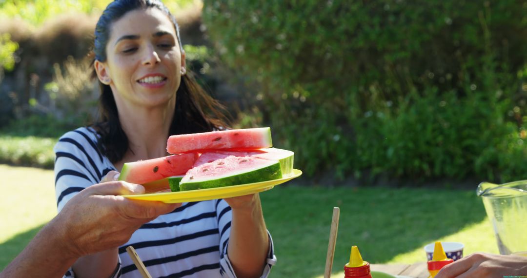 A young Caucasian woman is offering slices of watermelon at an outdoor gathering, with copy space - Free Images, Stock Photos and Pictures on Pikwizard.com