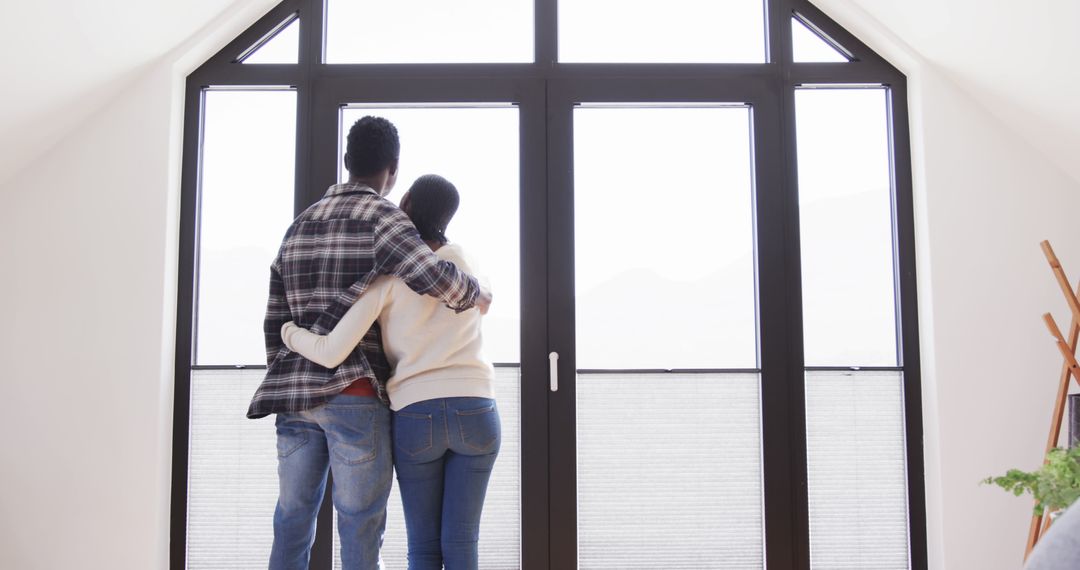 Couple Embracing and Looking Out Sunny Window at Home