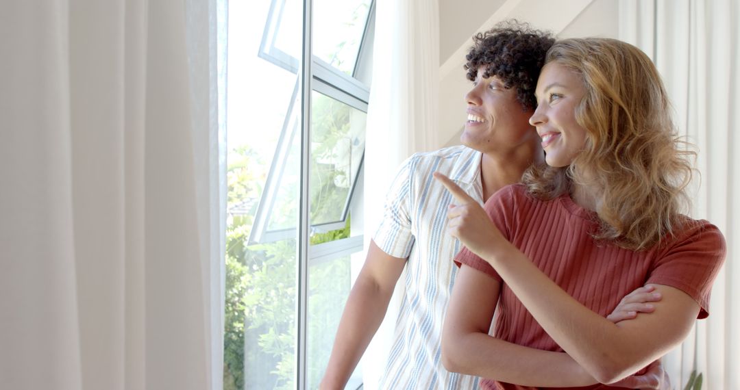 Happy Couple Enjoying View Through Large Window in Modern Living Room
