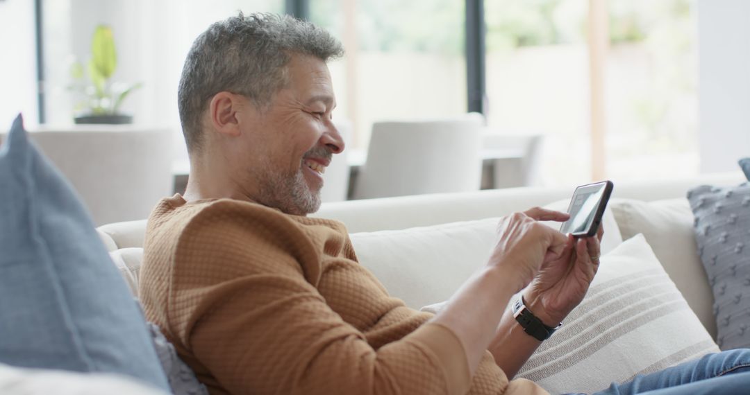 Middle-aged Man Smiling While Using Smartphone on Couch - Free Images, Stock Photos and Pictures on Pikwizard.com