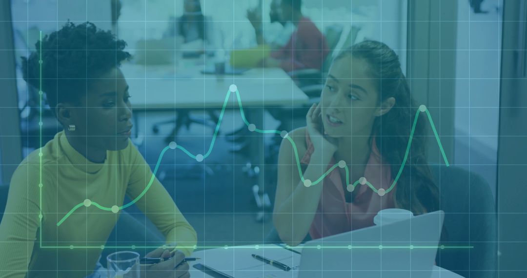 Two Women Discussing Data Insights with Graph Overlay in Office