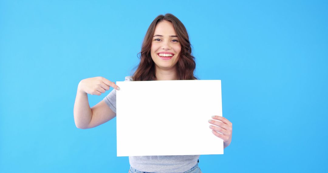 Smiling Woman Holding and Pointing at Blank Sign on Blue Background - Free Images, Stock Photos and Pictures on Pikwizard.com