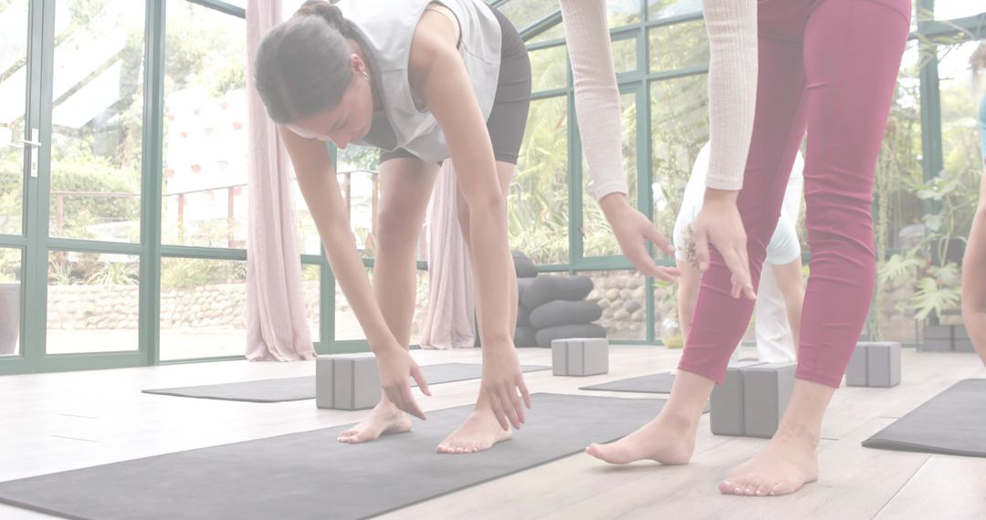 Women Practicing Forward Fold in Bright Glass Yoga Studio with Mats, Blocks, Bolsters