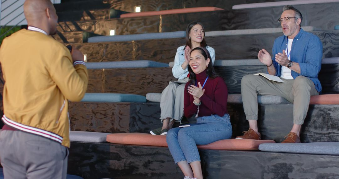 Diverse Team Applauding Presenter in Modern Workspace with Tiered Seating and Notebooks