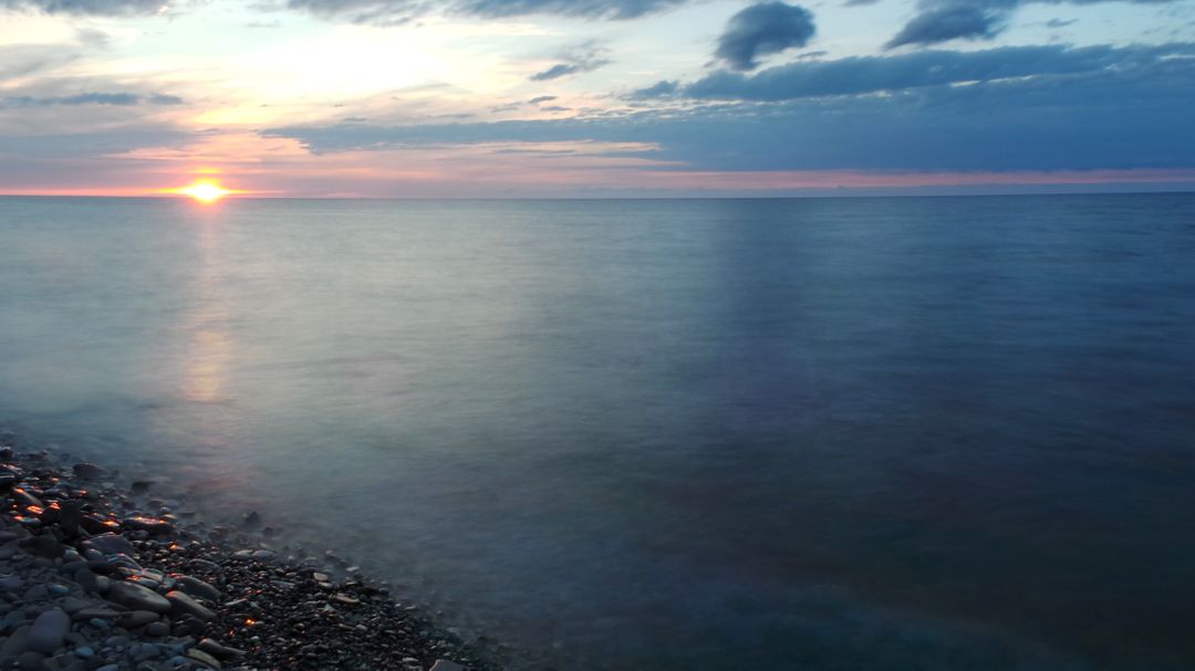 Tranquil Sunset Over Calm Ocean with Rocky Shores - Free Images, Stock Photos and Pictures on Pikwizard.com