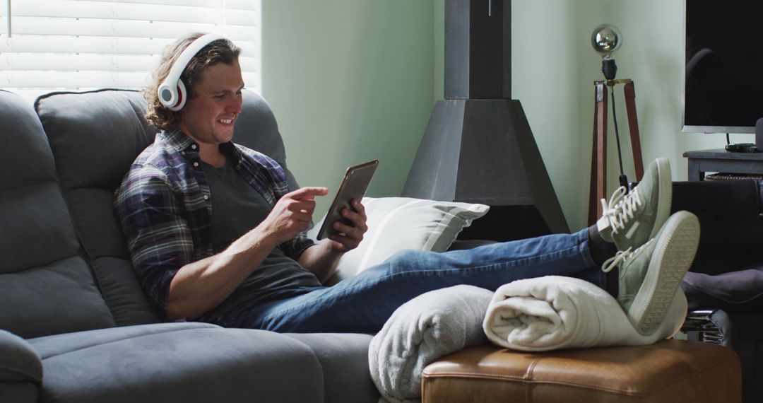 Young Man Relaxing on Couch with Tablet and Headphones - Free Images, Stock Photos and Pictures on Pikwizard.com