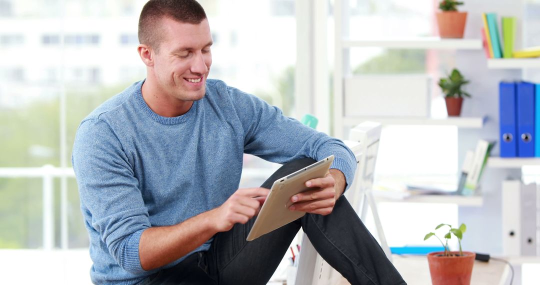 Young man smiling and using tablet in bright modern office - Free Images, Stock Photos and Pictures on Pikwizard.com