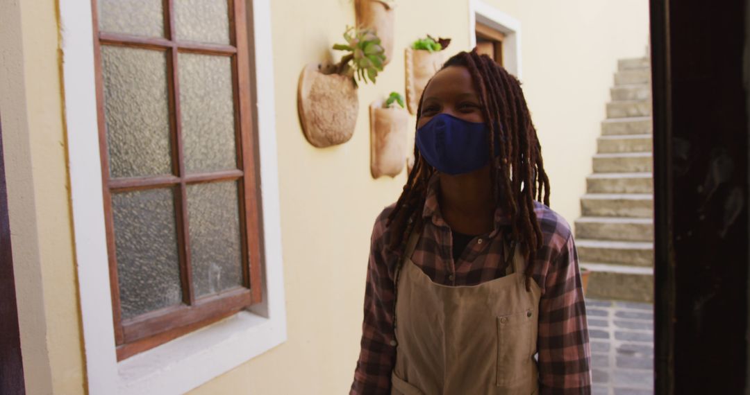 Female Florist Wearing Apron and Mask Standing by Doorway - Free Images, Stock Photos and Pictures on Pikwizard.com