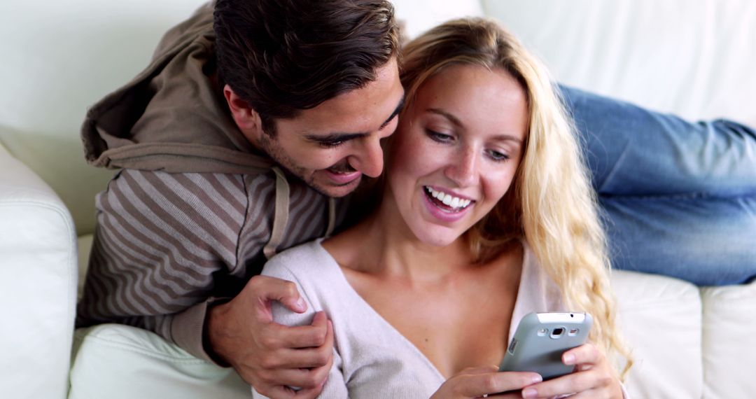 Happy Couple Smiling Together on Couch with Smartphone