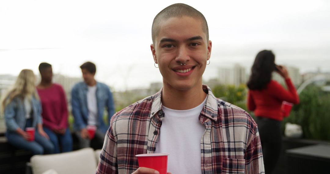 Smiling Young Man Holding Cup at Rooftop Party - Free Images, Stock Photos and Pictures on Pikwizard.com