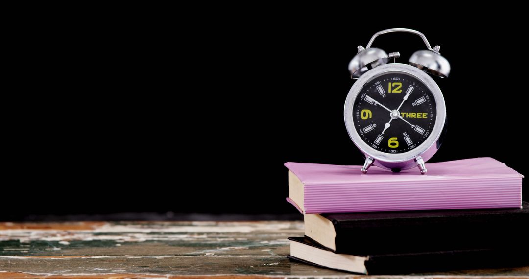 An alarm clock sits atop a stack of books against a dark background, with copy space - Free Images, Stock Photos and Pictures on Pikwizard.com