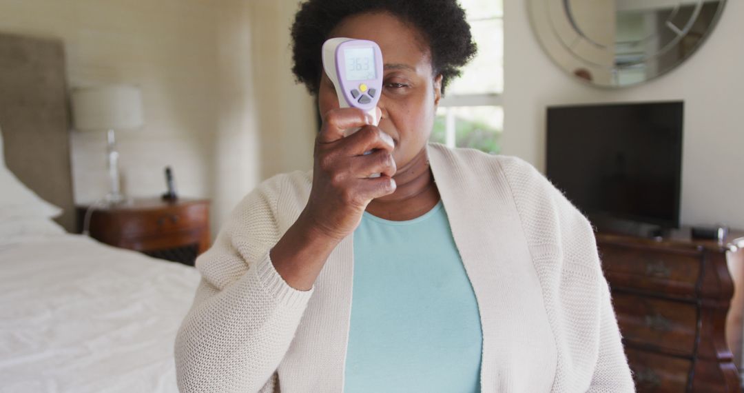 African American Woman Using Infrared Thermometer at Home - Free Images, Stock Photos and Pictures on Pikwizard.com