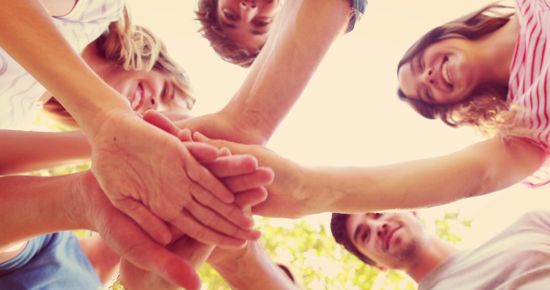 A group of smiling youths stack hands in a sunlit setting, symbolizing unity and teamwork. - Free Images, Stock Photos and Pictures on Pikwizard.com