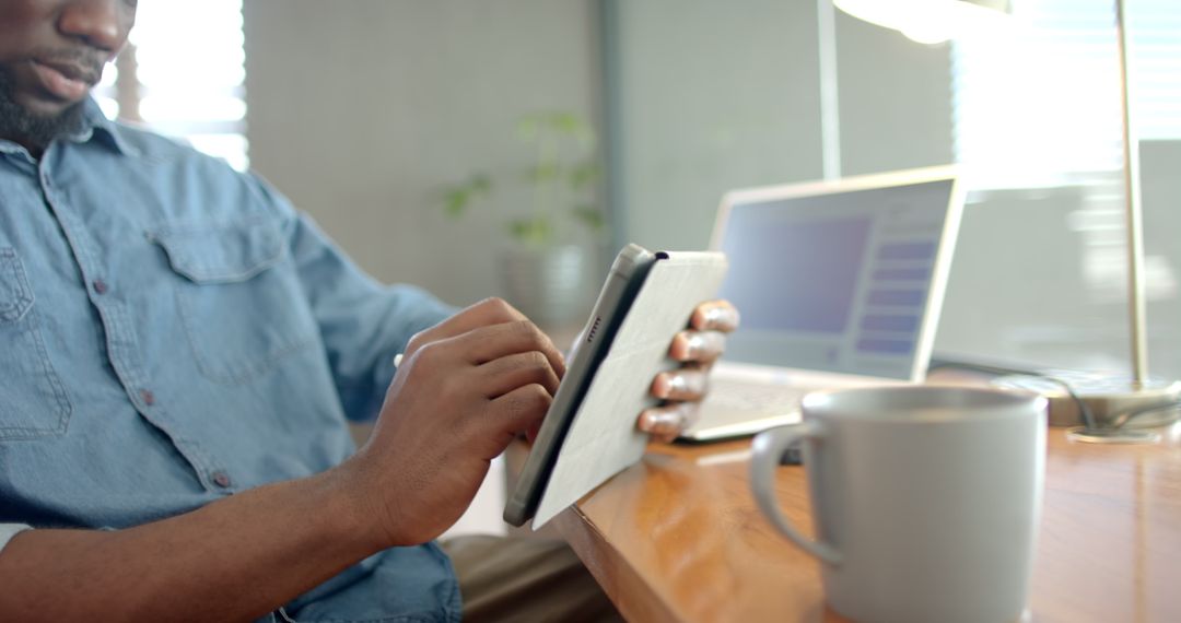 Professional Using Tablet Next to Laptop and Coffee Mug in Office