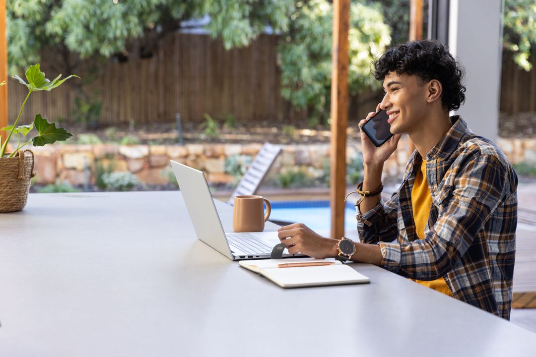 Young Man Using Laptop Outdoors While Talking on Smartphone