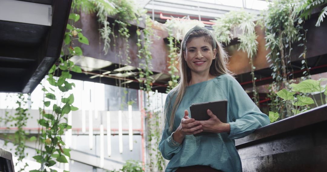 Smiling businesswoman holding tablet in modern office with plants design - Free Images, Stock Photos and Pictures on Pikwizard.com