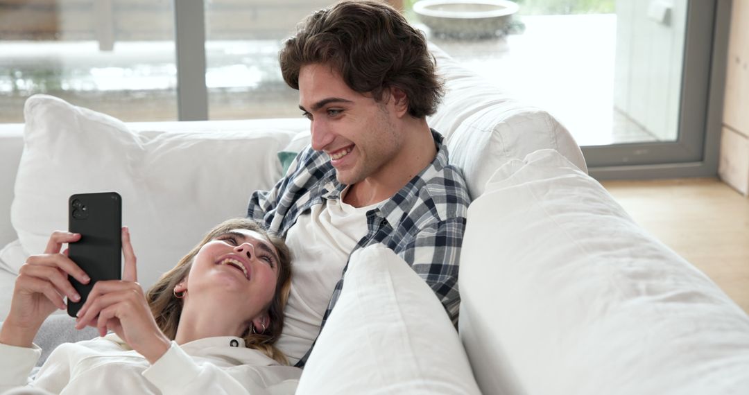 Couple Enjoying Leisure Time with Smartphone on White Sofa at Home