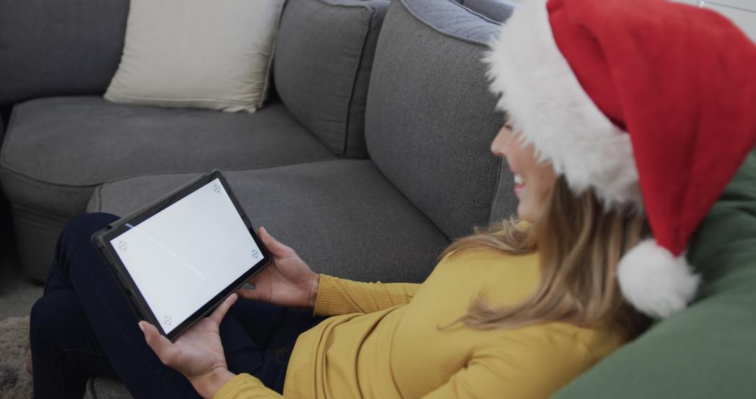 Woman Wearing Santa Hat Browsing Tablet at Home during Christmas - Free Images, Stock Photos and Pictures on Pikwizard.com